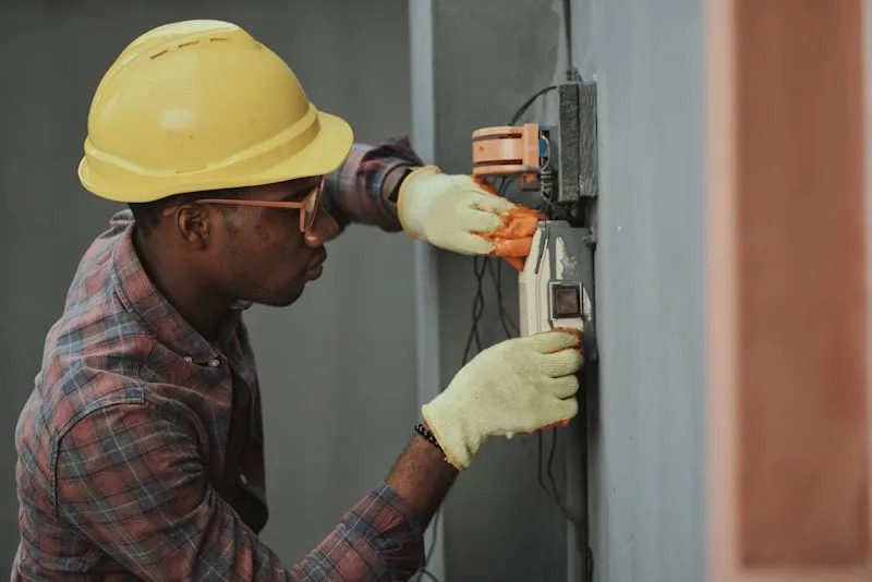 Electrician wearing safety helmet and gloves repairing electrical wiring on a wall switch panel
